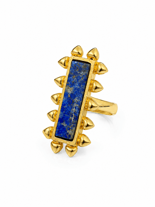 Close-up of AZRAQ ring showing its elongated blue lapis stone, gold-tone heart-stud edging and band on white.