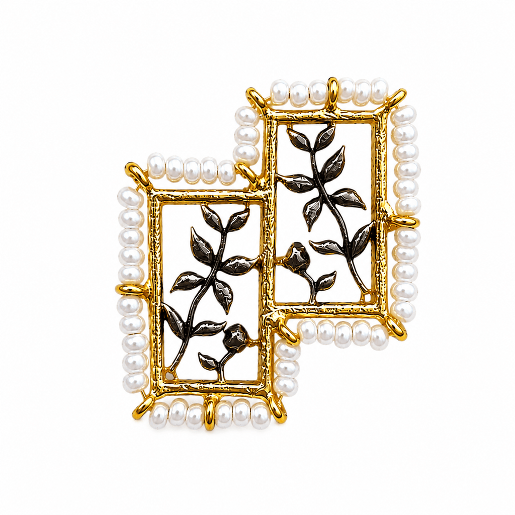 Close-up of FARSI ring showing offset gold-tone frames, white pearl edging and dark branch-and-leaf details on white.