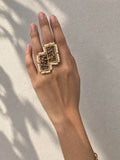 FARSI statement ring with twin gold-tone rectangular frames, white pearl borders and dark leafy motifs, worn on a hand.