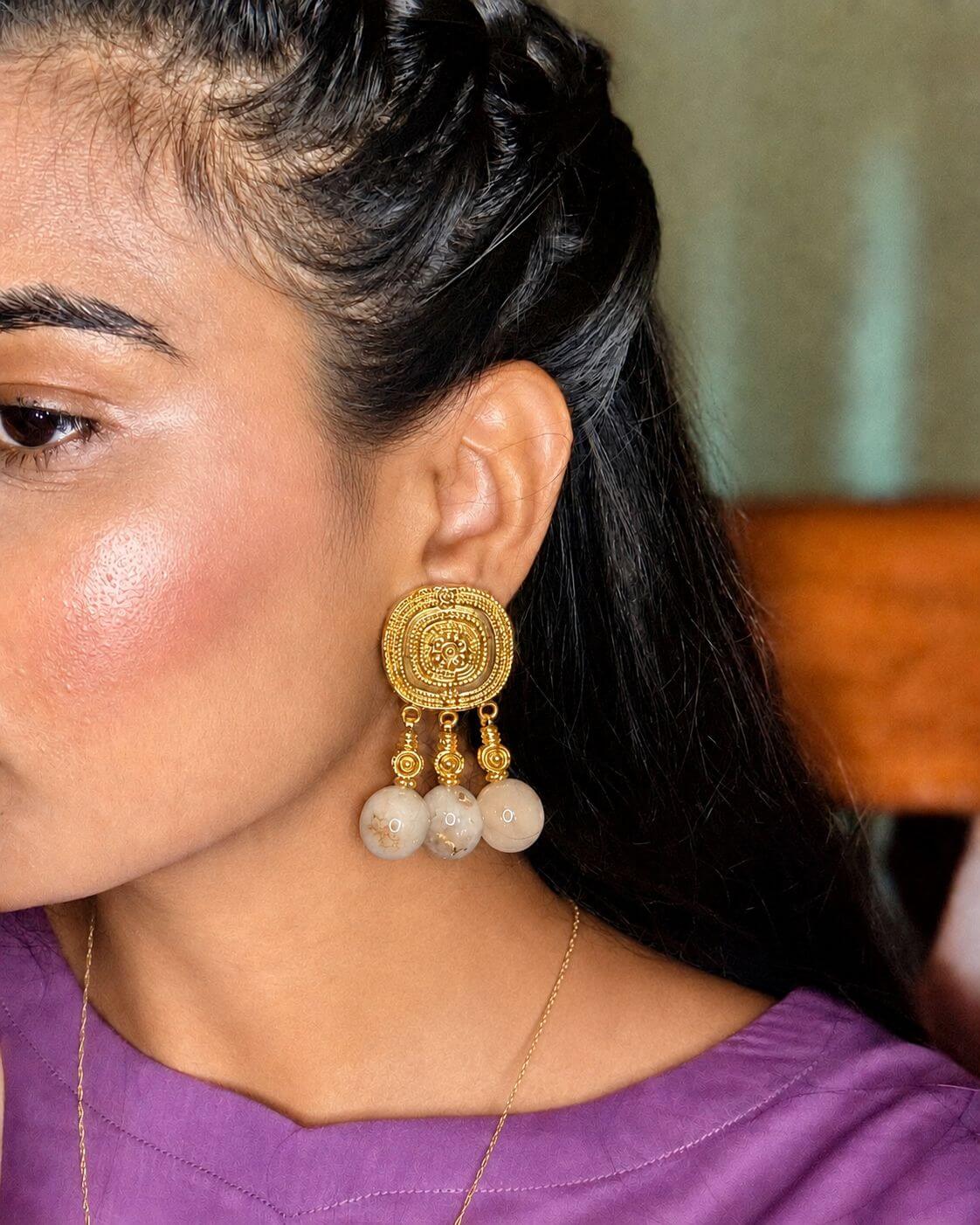 GOHAR statement earring worn on an ear, showing an ornate gold-tone stud and three dangling cream beads.