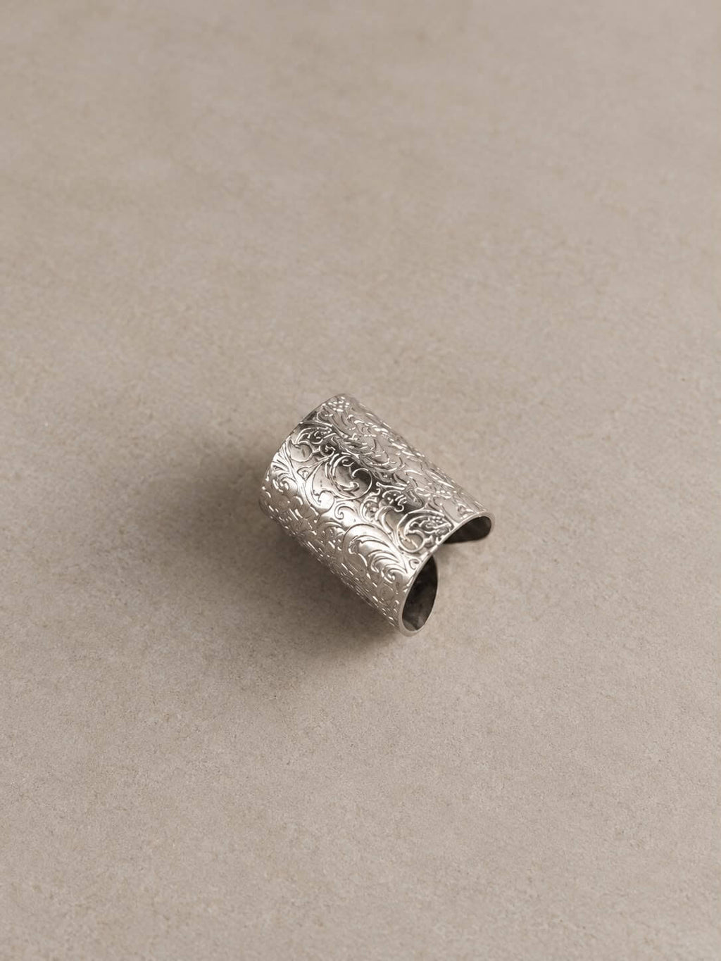 MEHRAB wide silver-tone ring with engraved floral scrollwork and an open-back band, displayed on beige.