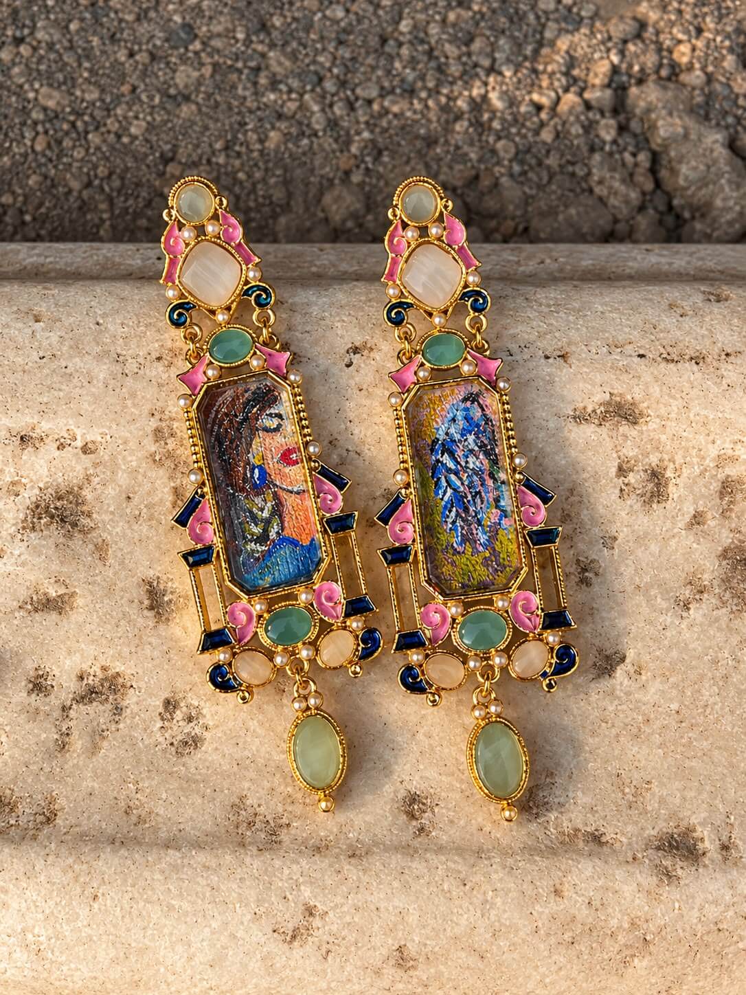 NIGAAR statement earrings with colourful portrait and bird panels, pink accents and pale green drops, displayed on stone.