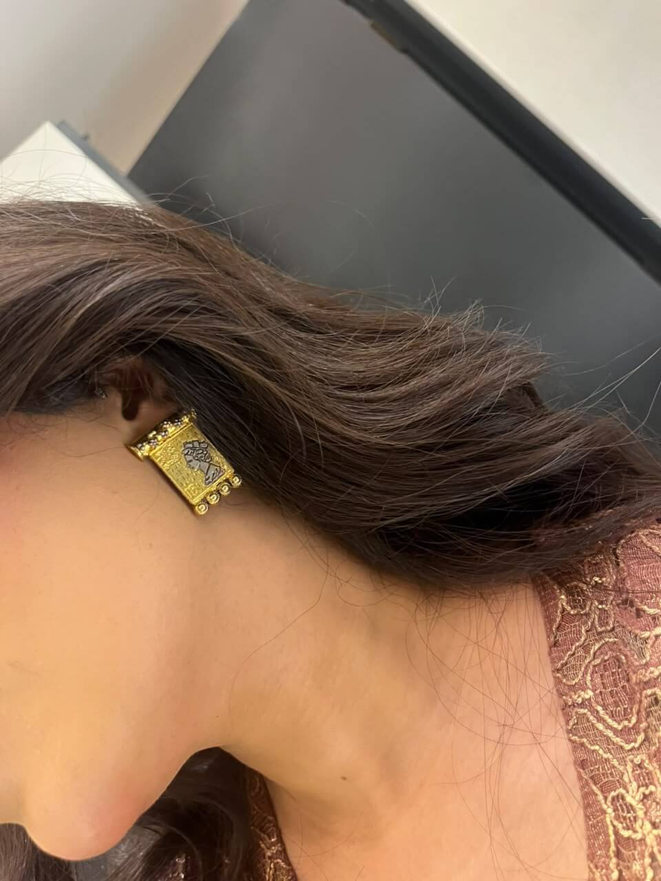 TALA rectangular statement earring worn on an ear, showing its gold-tone finish, dark portrait motif and beaded edge.