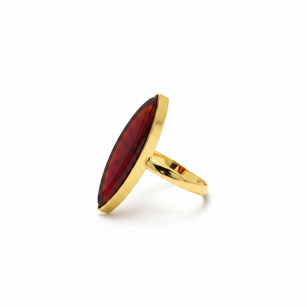 Side view of MEHR ring showing its faceted red marquise-shaped centre, gold-tone setting and slim band on white.